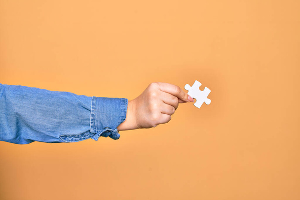 Hand of caucasian young woman holding piece of puzzle over isolated yellow background - Photo, Image