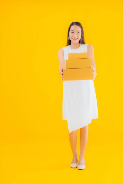 Portrait beautiful young asian woman with parcel box on yellow isolated background - Valokuva, kuva