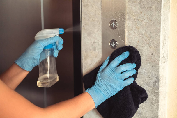Manos en guantes de goma azul limpiando y desinfectando los botones del ascensor usando spray desinfectante de alcohol. Antiséptico, desinfección, cuidado de la salud. - Foto, Imagen
