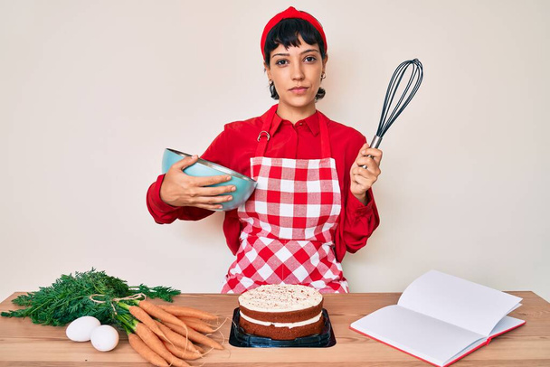 Kaunis brunettte nainen ruoanlaitto porkkana kakku käyttäen vispilä rento vakava ilme kasvot. yksinkertainen ja luonnollinen kameraan katsominen.  - Valokuva, kuva