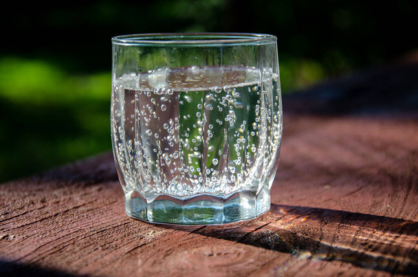 Szklanka z wodą mineralną, gazowaną na drewnianej desce w ogrodzie. - Zdjęcie, obraz