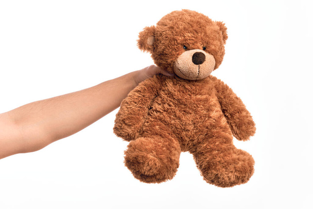Hand von kaukasischen jungen Mann hält niedlichen braunen Teddybär Puppe über isolierten weißen Hintergrund - Foto, Bild