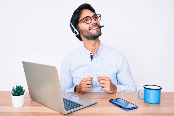 Komea latino mies työskentelee toimistossa yllään operaattori kuulokkeet haluavat sivulle, rentoutua profiili aiheuttaa luonnolliset kasvot ja luottavainen hymy.  - Valokuva, kuva
