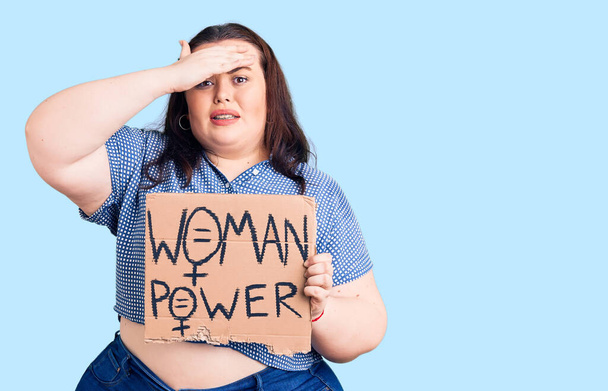 Young plus size woman holding woman power banner stressed and frustrated with hand on head, surprised and angry face  - Photo, Image