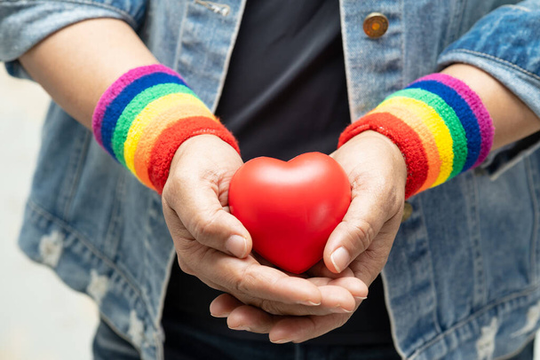 ゲイ、レズビアン、バイセクシャル、トランスジェンダー、人権の6月の社会では、虹のリストバンドを身に着けているアジアの女性と赤いハート、 LGBTの誇りの月の象徴を祝う. - 写真・画像