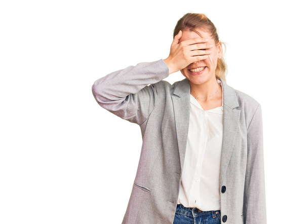 Young beautiful blonde woman wearing elegant jacket smiling and laughing with hand on face covering eyes for surprise. blind concept.  - Photo, Image