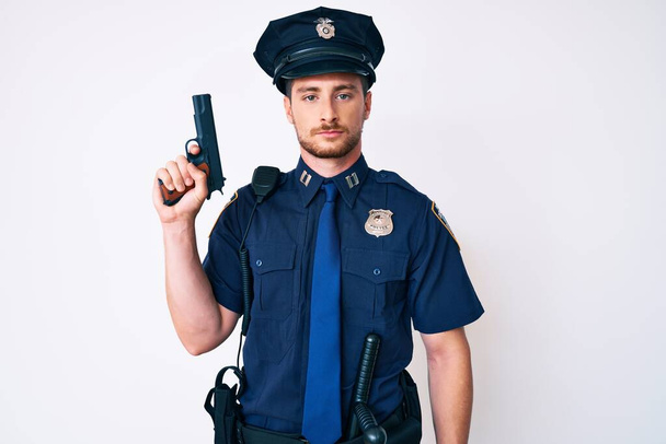Молодий білий чоловік у поліцейській формі тримає пістолет мислення ставлення і тверезий вираз, дивлячись на себе впевнено
  - Фото, зображення