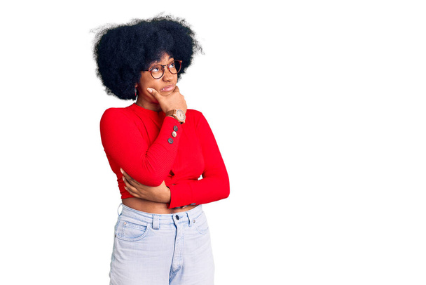 Jeune fille afro-américaine portant des vêtements décontractés et des lunettes pensant inquiet d'une question, préoccupé et nerveux avec la main sur le menton  - Photo, image
