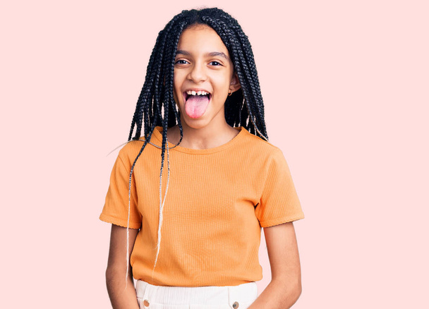 Linda chica afroamericana vistiendo ropa casual sacando la lengua feliz con expresión divertida. concepto de emoción.  - Foto, imagen