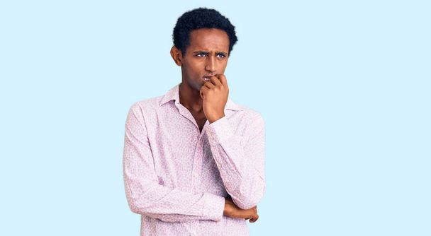 Afrikaanse knappe man draagt casual roze shirt kijken gestrest en nerveus met handen op de mond bijtende nagels. angstprobleem.  - Foto, afbeelding
