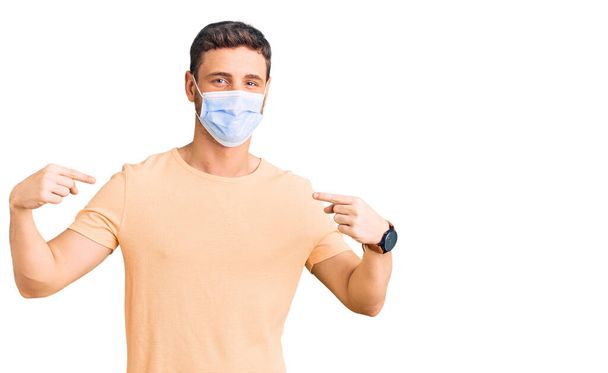 Handsome young man with bear wearing medical mask for coronavirus looking confident with smile on face, pointing oneself with fingers proud and happy.  - Photo, Image