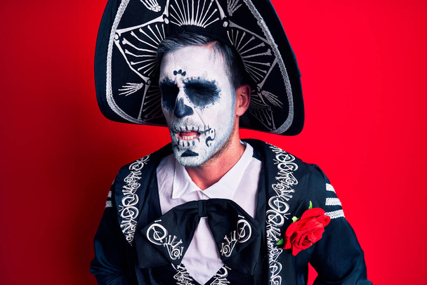 Молодой человек, одетый в мексиканский день мертвого костюма поверх красного с рукой на животе, потому что тошнота, болезненная болезнь чувствует себя нехорошо. Концепция.  - Фото, изображение