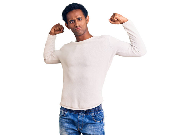 Afroamerykanin przystojny mężczyzna ubrany w luźny zimowy sweter pokazujący mięśnie rąk uśmiechnięte dumą. koncepcja sprawności.  - Zdjęcie, obraz