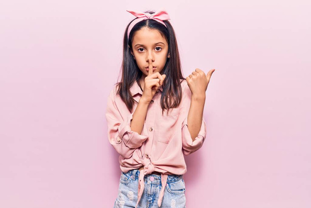 Beautiful child girl wearing casual clothes asking to be quiet with finger on lips pointing with hand to the side. silence and secret concept.  - Fotoğraf, Görsel