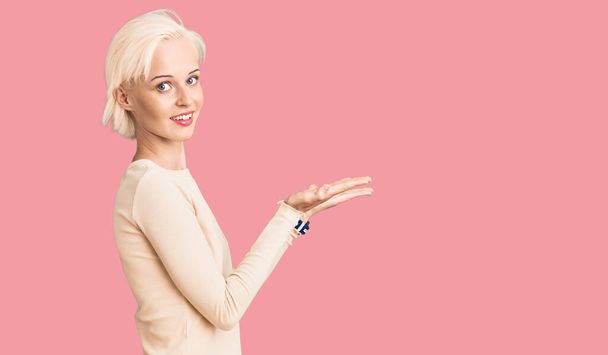 Молодая блондинка в повседневной одежде, указывая в сторону с открытыми руками ладонями показывая пространство для копирования, представляя рекламу улыбаясь взволнованной счастливой  - Фото, изображение