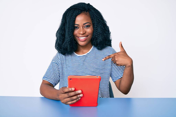 Belle femme africaine à l'aide d'un dispositif tactile pointant du doigt un sourire heureux et fier  - Photo, image