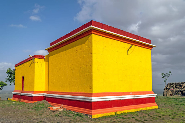 Helder geel en rood geschilderd Dhavaleshwar tempel met mooie blauwe lucht, gelegen op Dhavalgad fort, Purandar in de buurt van Pune, Maharashtra, India. - Foto, afbeelding