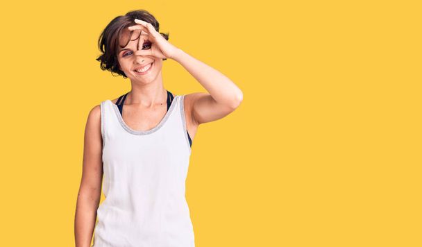 Beautiful young woman with short hair wearing casual sport clothes smiling happy doing ok sign with hand on eye looking through fingers  - Foto, Imagem