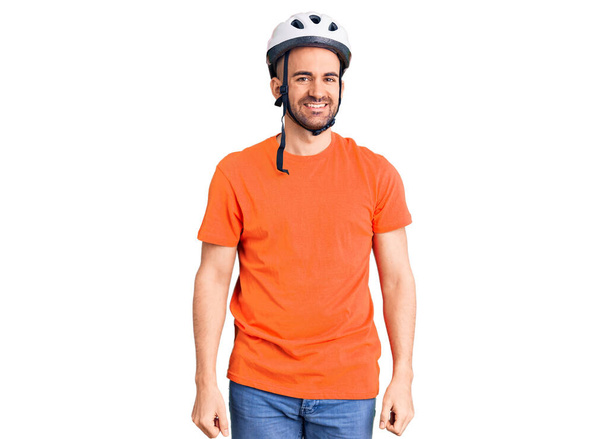 Jeune bel homme portant un casque de vélo regardant positif et heureux debout et souriant avec un sourire confiant montrant les dents  - Photo, image