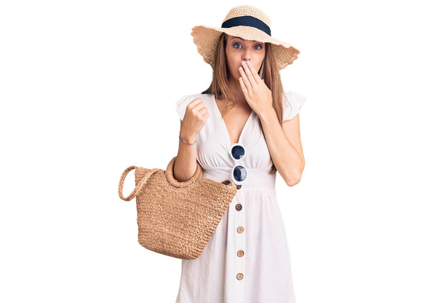 Young beautiful blonde woman wearing summer dress and wicker handbag covering mouth with hand, shocked and afraid for mistake. surprised expression  - Foto, Bild