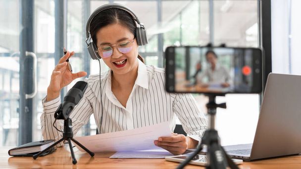 Азійські жінки подкастинг і онлайн ток-шоу в студії за допомогою навушників, професійного мікрофона і комп'ютерного ноутбука за столом дивлячись на камеру для радіоподкасту. - Фото, зображення