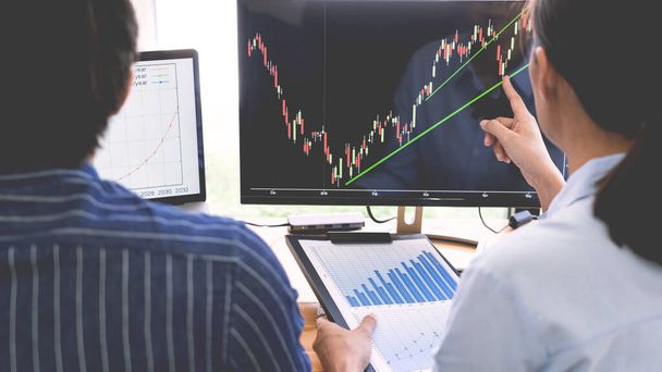 брокер показывает некоторые восходящие к его коллеге планирования и анализа графика торговли на фондовом рынке с данными фондового графика на нескольких экранах компьютера - Фото, изображение