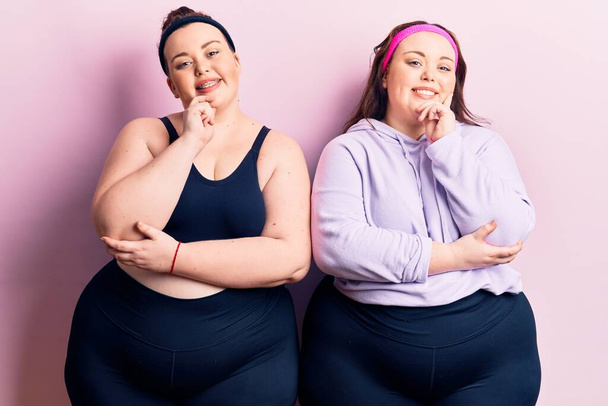 Young plus size twins wearing sportswear looking confident at the camera with smile with crossed arms and hand raised on chin. thinking positive.  - Zdjęcie, obraz