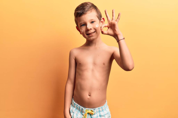 Aranyos szőke gyerek visel fürdőruha csinál oké jel ujjakkal, mosolygós barátságos gesztus kiváló szimbólum  - Fotó, kép