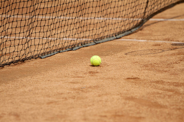 Close up tennis ball and net on court. Close up of tennis ball on clay court. Red clay court. - Fotografie, Obrázek
