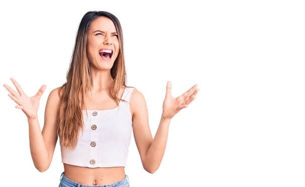 Young beautiful girl wearing casual sleeveless t shirt crazy and mad shouting and yelling with aggressive expression and arms raised. frustration concept.  - Foto, Imagem
