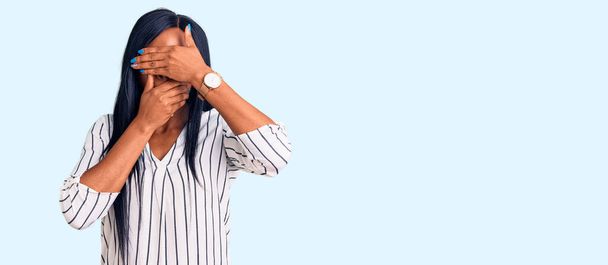 Genç Afro-Amerikalı kadın günlük kıyafetler ve gözlük takıyor gözlerini ve ağzını elleriyle kapatıyor, şaşırmış ve şok olmuş. duygu gizleme  - Fotoğraf, Görsel