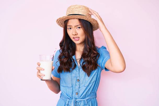 Yazlık şapka takan genç, güzel Çinli kız elinde bir bardak sütle gergin ve hayal kırıklığına uğramış, şaşırmış ve kızgın bir yüz.  - Fotoğraf, Görsel