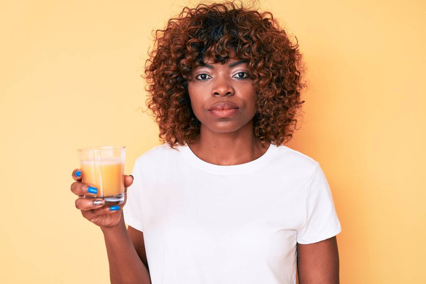 Młoda Afroamerykanka pije szklankę soku pomarańczowego myśląc nastawienie i trzeźwy wyraz twarzy patrząc pewny siebie  - Zdjęcie, obraz