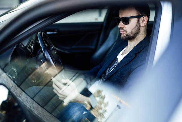 Módní bohatý muž se dívá na telefon a sedí v autě - Fotografie, Obrázek