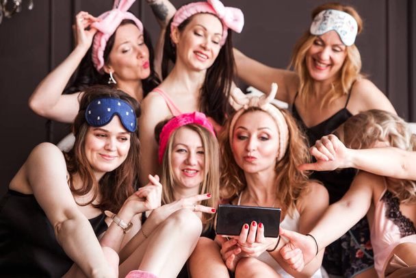 Molte ragazze ragazze hanno organizzato un pigiama party su un letto di peluche. Le ragazze sorridono, guardano la telecamera e si fanno un selfie. Foto orizzontale - Foto, immagini