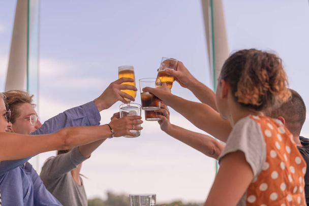 A group of young people raising their drinks for a toast on an out of focus background. Friendship and lifestyle concept. - Foto, Imagen