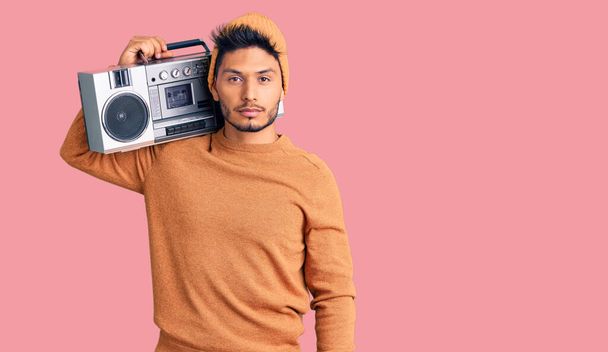 Handsome latin american young man holding boombox, listening to music relaxed with serious expression on face. simple and natural looking at the camera.  - Photo, Image