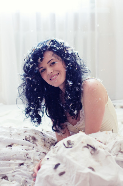 Smiling young woman with feathers on a bed - Фото, изображение