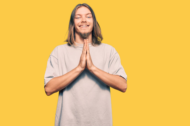 Handsome caucasian man with long hair wearing casual clothes praying with hands together asking for forgiveness smiling confident.  - Fotografie, Obrázek