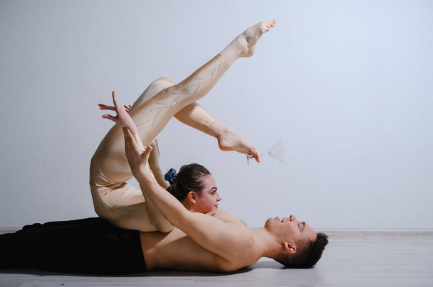 Acrobatic couple perform number on a white background. A duet of gymnasts rehearsing a performance with support. A man and a very flexible woman are dancing. - Foto, Imagem