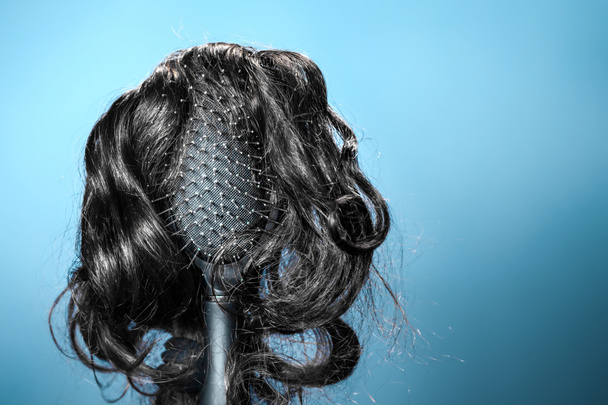 女性の髪。黒いウィッグ付きの黒いヘアブラシは、ヘアスタイルの女性の頭のように見えます。青の背景。コピースペース。美容室、ヘアケア、ヘア移植の概念. - 写真・画像