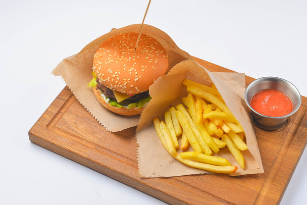 Hamburger with french fries and tomato dip sauce. Fast food, junk food concept. Served on a rustic wooden board over white background. Close up. - Foto, imagen