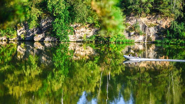 Σκάφος στο ποτάμι με αντανάκλαση. Μια γραφική φθινοπωρινή άποψη των πολύχρωμων φυλλωμάτων του δάσους που αντανακλά σε μια λίμνη. Ένα πλοίο διασχίζει τον ποταμό με φθινοπωρινό χρώμα. Πράσινα φύλλα - Φωτογραφία, εικόνα
