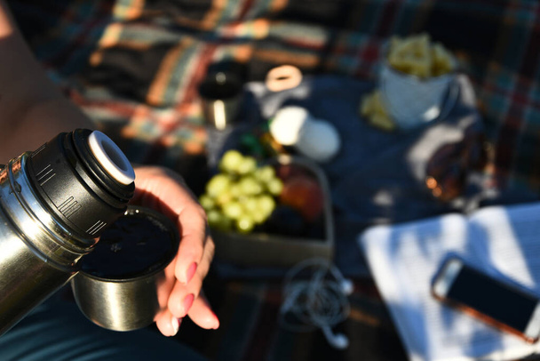 Traveler pouring hot tea from thermos to cup at autumn fallen forest outdoor. Summer autumn picnic. Copy space - Photo, Image