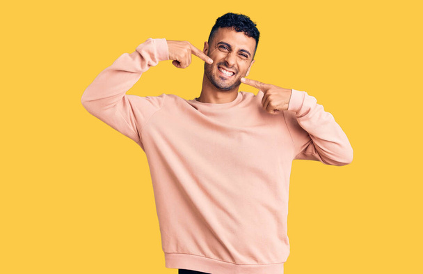 Young hispanic man wearing casual clothes smiling cheerful showing and pointing with fingers teeth and mouth. dental health concept.  - Foto, immagini