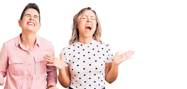 Δύο γυναίκες που φορούν καθημερινά ρούχα γιορτάζοντας τρελός και τρελός για την επιτυχία με τα χέρια ψηλά και κλειστά μάτια ουρλιάζοντας ενθουσιασμένος. έννοια νικητή  - Φωτογραφία, εικόνα