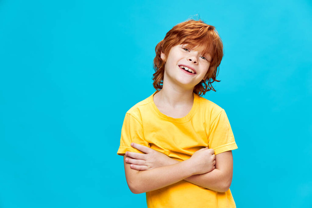 child with red hair has his arms crossed over his chest and smiles against Copy Space - Фото, изображение