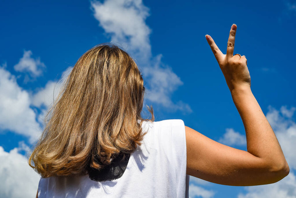 the girl against the sky with her back to the camera depicts a victory hand - Photo, Image