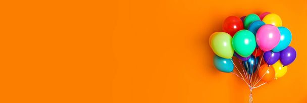 Bunch of bright balloons on orange background, space for text. Banner design  - Zdjęcie, obraz
