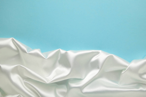White satin fabric on blue background. Top view - Zdjęcie, obraz